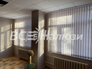 Светло-серые вертикальные жалюзи на двух окнах, солнце сквозь ламели