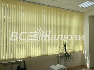 Светло-жёлтые вертикальные жалюзи на широком окне кабинета