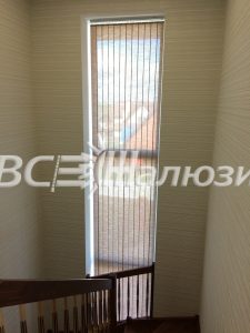 Кремовые вертикальные жалюзи на узком высоком окне лестницы