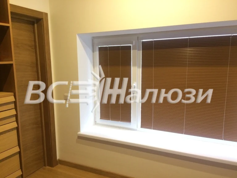 Коричневые горизонтальные жалюзи на широком окне рядом со шкафом