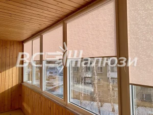 Персиковые рулонные шторы подняты на окнах застеклённого балкона