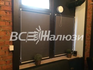 Тёмно-серые рулонные шторы, слева кирпичная стена и часы