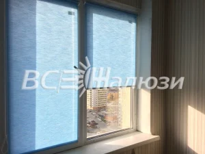 Голубые рулонные шторы, одно полотно поднято, вид на город