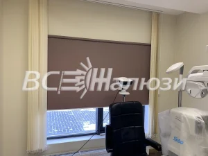 Коричневая рулонная штора на окне кабинета с креслом и кушеткой