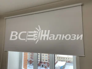 Белая рулонная штора приспущена, за окном зимний двор