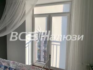 Белые рулонные шторы подняты на балконной двери, рядом полог