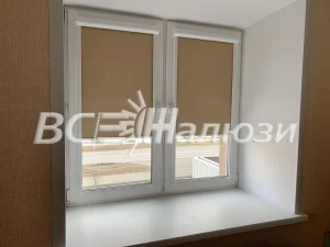 Карамельные рулонные шторы приподняты на окне пустой комнаты