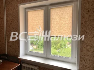 Персиковые узорчатые рулонные шторы приподняты, за окном сад