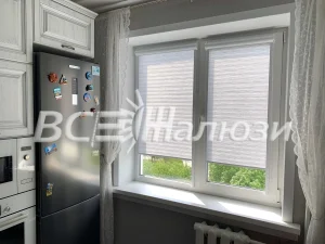 Светлые полосатые рулонные шторы подняты на окне возле холодильника