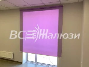 Сиреневая рулонная штора приспущена на окне офисного кабинета