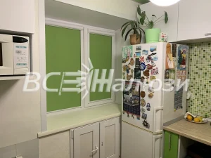 Зелёные рулонные шторы на кухонном окне рядом с холодильником