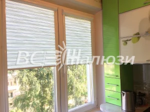 Белые рулонные шторы в полоску на окне кухни с зелёными фасадами