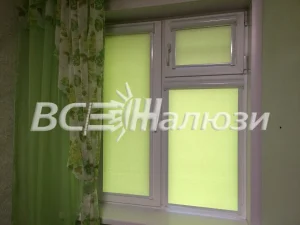 Салатовые рулонные шторы на окне рядом с зелёной занавеской