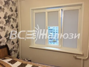 Серые рулонные шторы на окне комнаты с кроватью и узорчатыми обоями