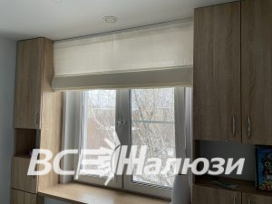 Кремовая римская штора над окном между шкафами светлого дерева