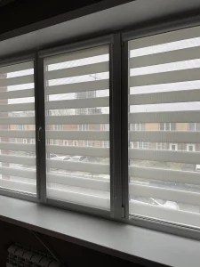Белые шторы зебра подняты наполовину, за окном улица