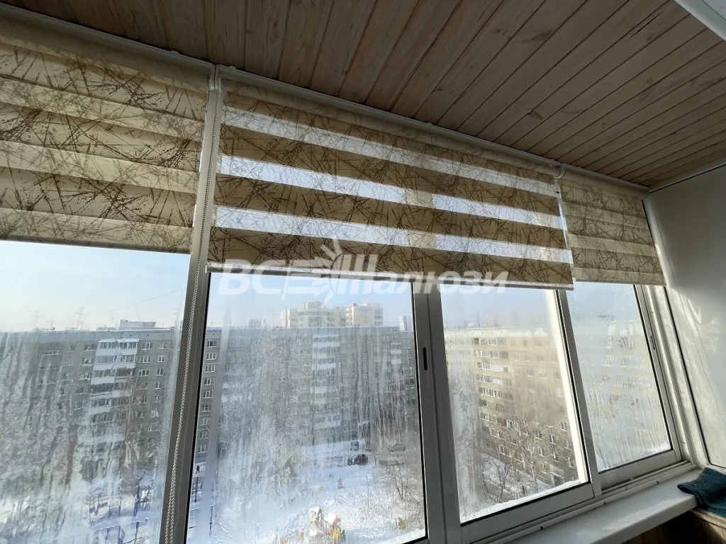 Бежевая штора зебра приспущена на окне балкона с деревянным потолком