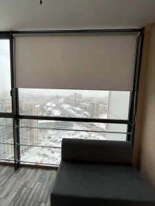 Бежевая рулонная штора на панорамном окне высокого этажа