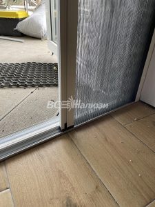 Нижняя часть дверной сетки у порога, слева деревянный пол