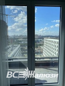 Москитная сетка плиссе на балконной двери, за окном крыши города