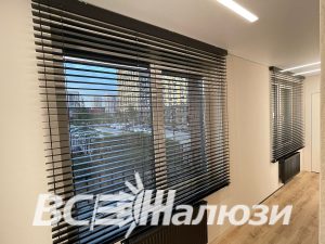 Коричневые жалюзи с приоткрытыми ламелями на широком офисном окне