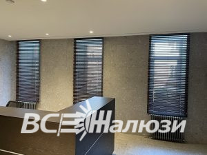 Три высоких окна с тёмно-коричневыми жалюзи в холле у стойки