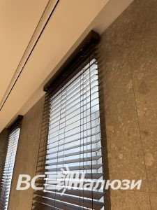 Вид снизу на тёмные жалюзи и карниз у мраморной стены