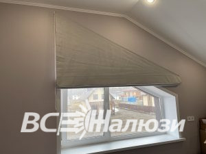 Оливковая римская штора собрана над скошенным окном мансарды