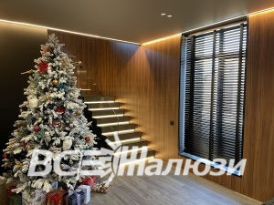 Тёмные жалюзи на высоком окне рядом с новогодней ёлкой