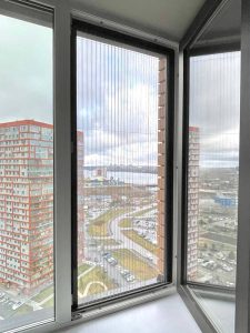 Сетка плиссе на панорамном окне квартиры, вид на город