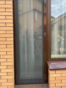 Одностворчатая сетка плиссе в дверном проёме кирпичного дома
